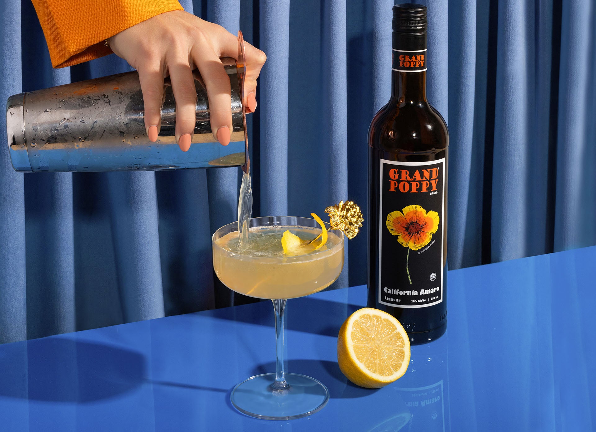 Hand pouring a margarita next to Grand Poppy Bottle