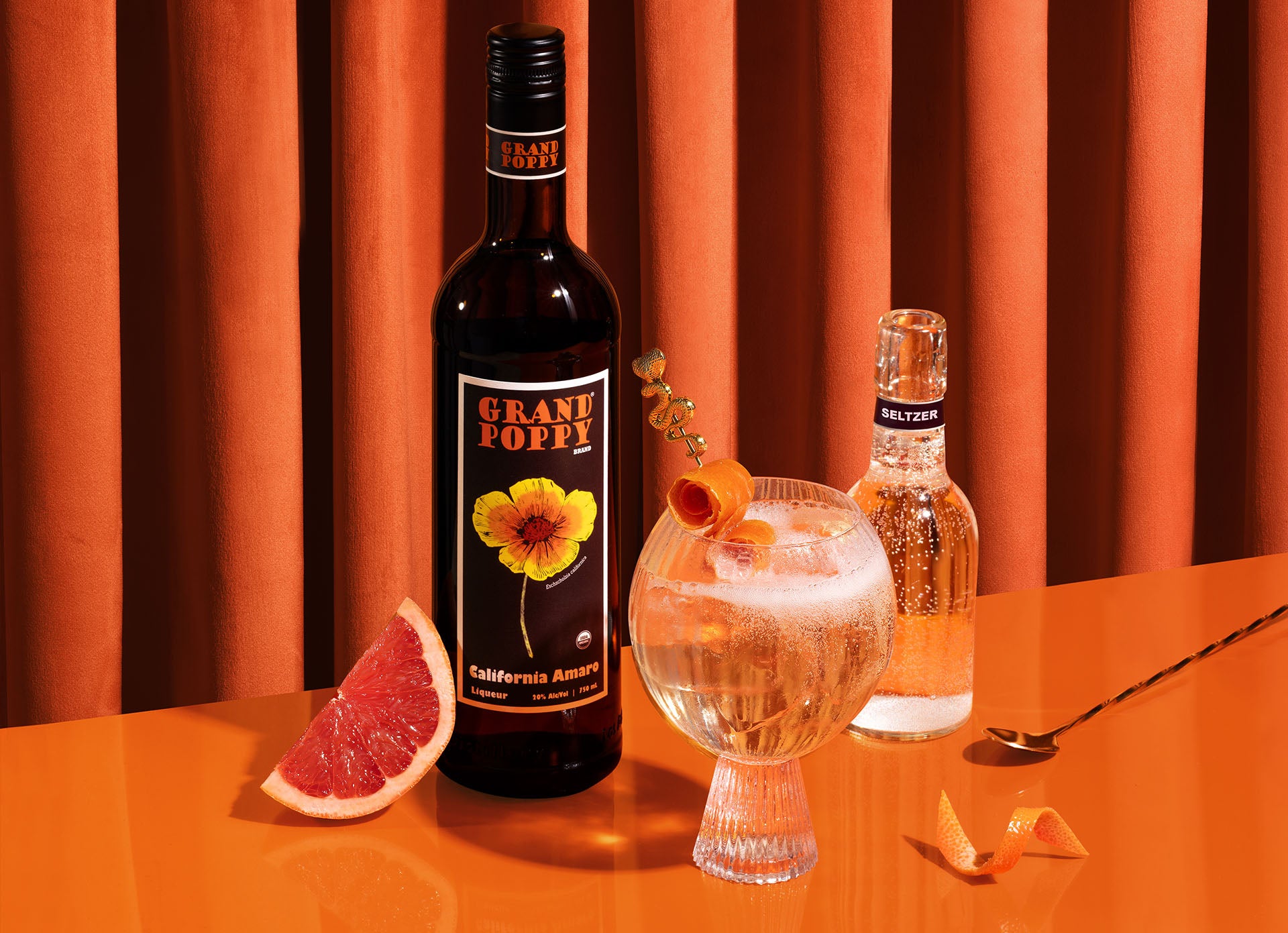 Bottle of Grand Poppy next to California spritz with fresh fruit and seltzer